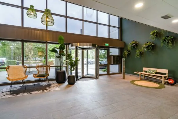 Moderne en sfeervol ingerichte entreehal aan de Baarnsche Dijk met veel groen, zitgelegenheid en een draaideur.